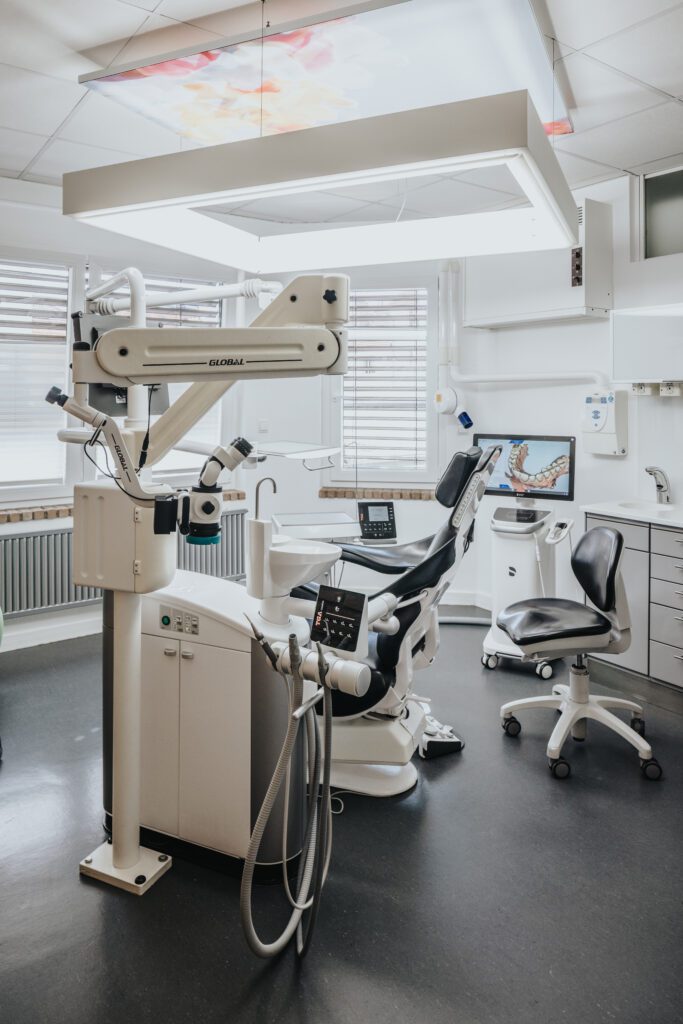 Voll ausgestattetes, modernes Behandlungszimmer bei Zahnarzt Dr. Fritz Kollmar in Kassel mit zahnmedizinischem Mikroskop, digitalem Scanner und ergonomischem Patientenstuhl vor einer rustikalen Backsteinwand.