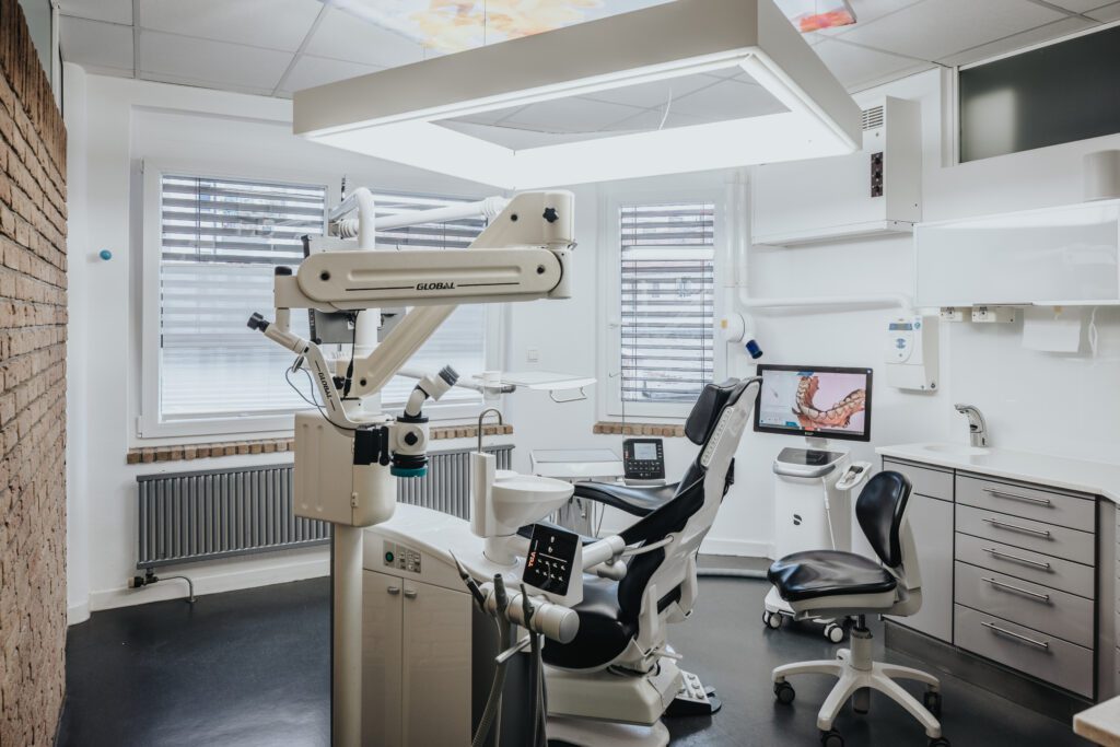 Voll ausgestattetes, modernes Behandlungszimmer bei Zahnarzt Dr. Fritz Kollmar in Kassel mit zahnmedizinischem Mikroskop, digitalem Scanner und ergonomischem Patientenstuhl vor einer rustikalen Backsteinwand.